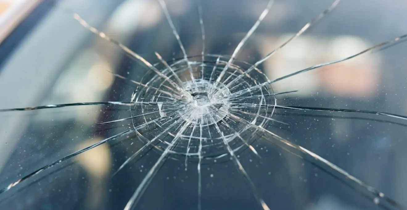 Détail macro d'un impact sur pare-brise avec texture du verre fissuré, illustrant les dégâts nécessitant une intervention